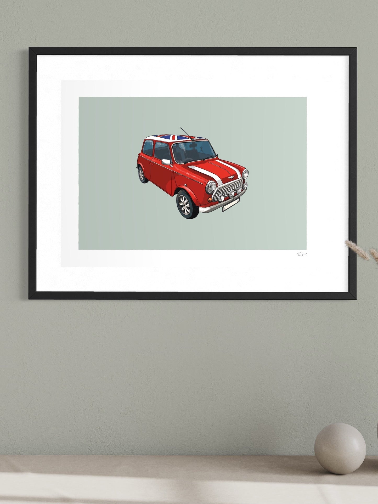 This image shows a giclee wall art print by Tom Laird Illustration of the British classic car, the Mini, framed in a beautiful living room with tasteful modern home decor. This art print of a red example with a Union Jack roof is available from Tom Laird Illustration in a variety of sizes.