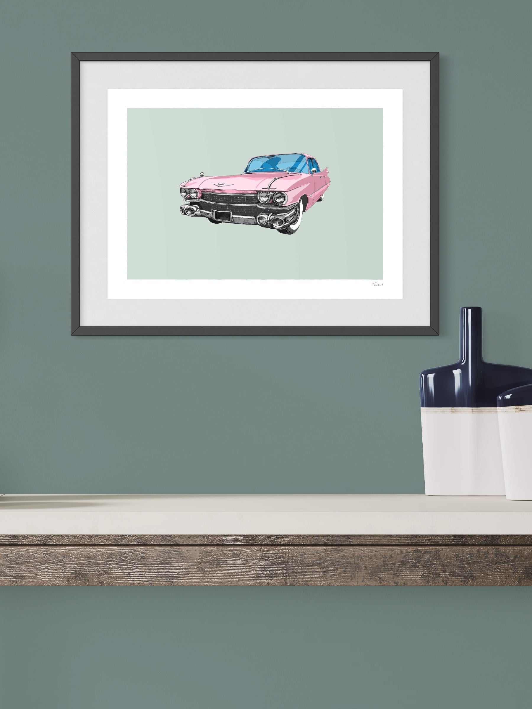 This image shows a giclee wall art print by Tom Laird Illustration of the American classic car, the Cadillac, framed in a beautiful living room with tasteful modern home decor. This art print of a pink example is available from Tom Laird Illustration in a variety of sizes.