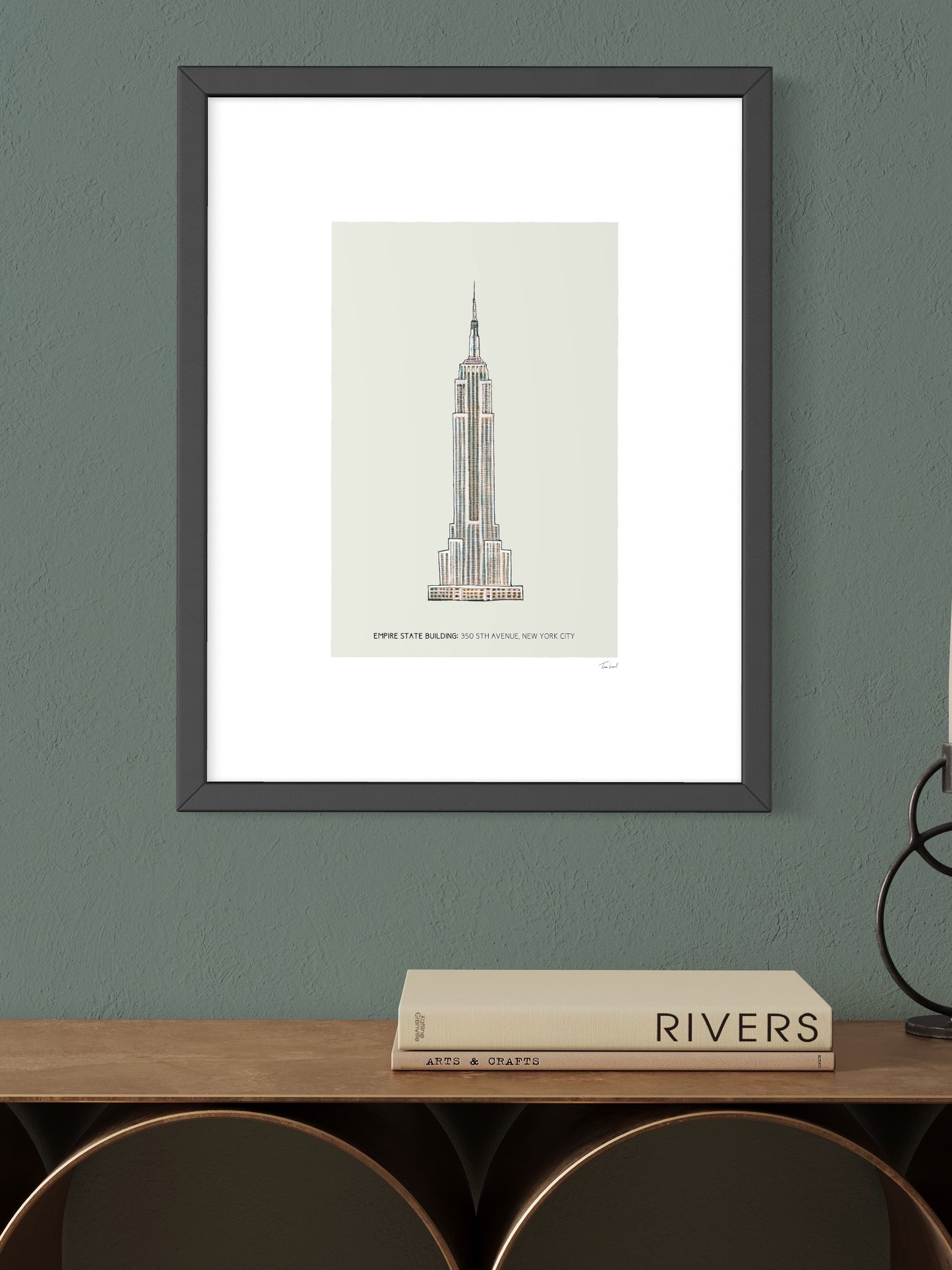 This image shows a giclee wall art print by Tom Laird Illustration of the world-famous New York City landmark the Empire State Building, framed in a beautiful living room with tasteful modern home decor. This art print is available from Tom Laird Illustration in A4 size.