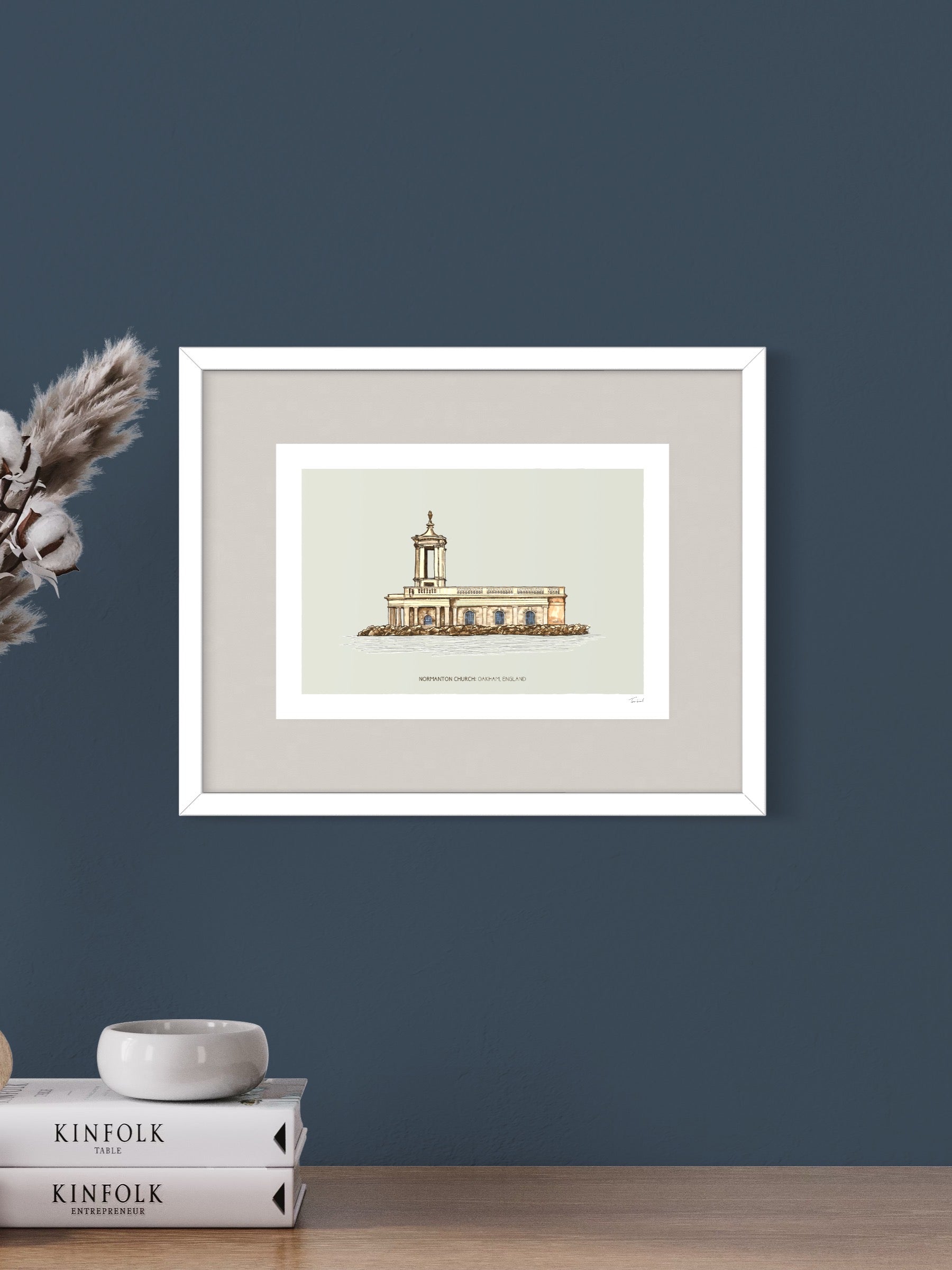 This image shows a giclee wall art print by Tom Laird Illustration of the unique English landmark and popular wedding venue Normanton Church, framed in a beautiful living room with tasteful modern home decor. This art print is available from Tom Laird Illustration in A4 size.